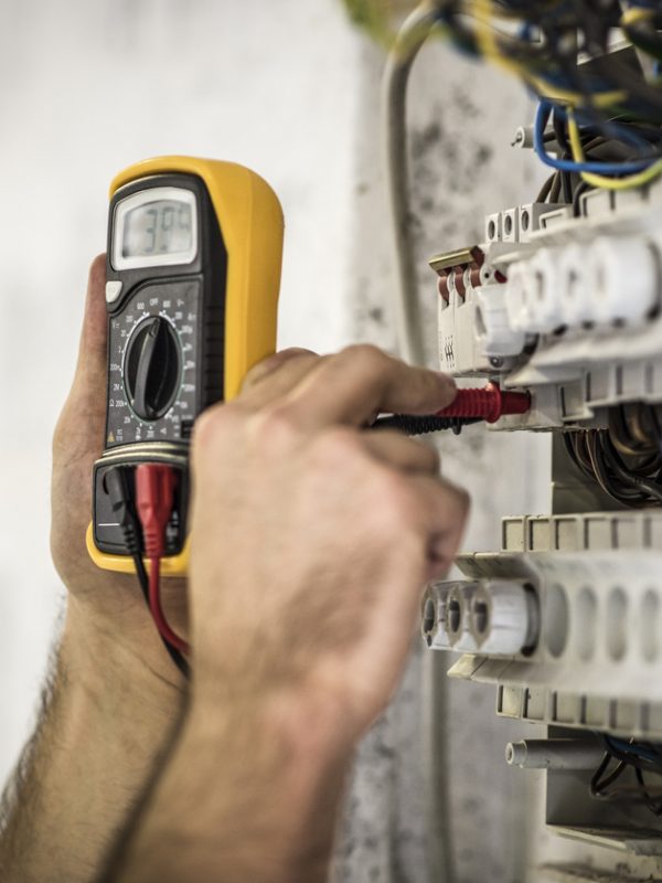 Detail shot of electrician testing voltage on a fuse box on construction site.
